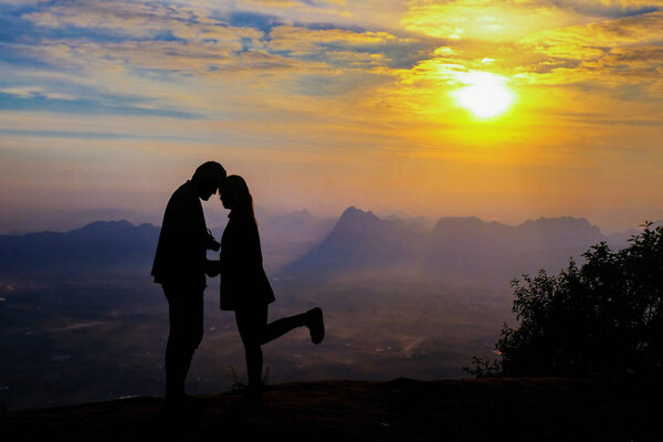Silhouette of happy young couple in love looking view sunset on the mountain. Romantic couple in love
