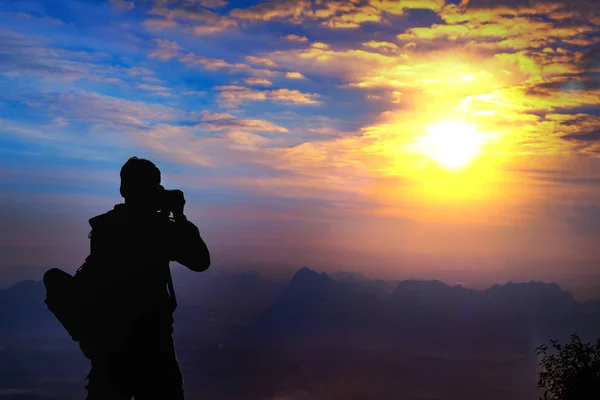 男性バックパッカーには、日没の backgro で彼女のデジタル一眼レフ カメラのシルエット — ストック写真