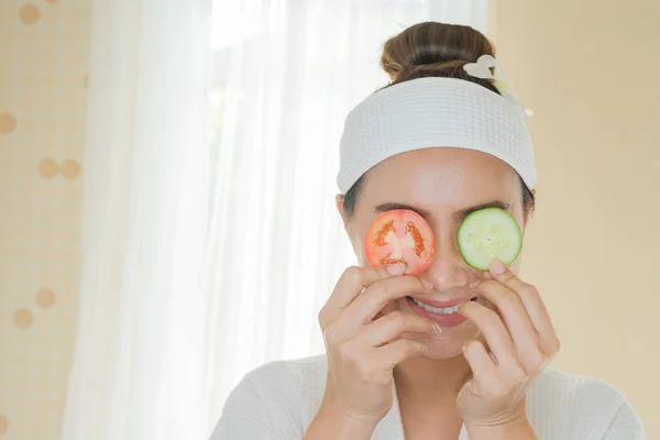 Mooie vrouw met een gezichtsmasker, met komkommers en tomaten op — Stockfoto