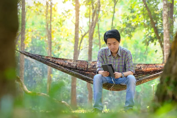 Erkek turistler ulusal parkta müzik dinleyerek hamakta dinleniyorlar.