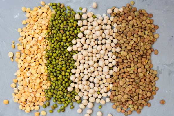 Variety of grains beans - mung, dry peas, lentils and chickpeas in jars on grey concrete background