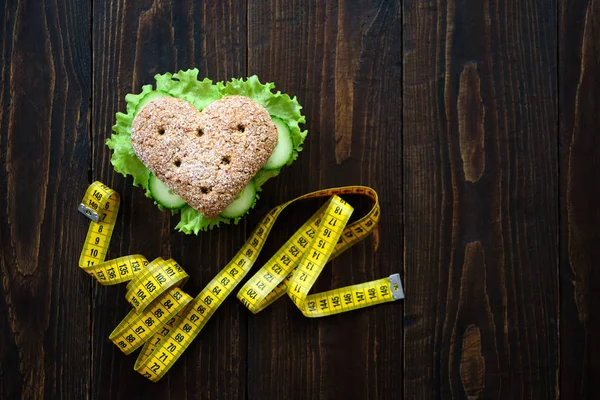 Healthy heart shape sandwich with salad and cucumbers. Dieting concept. Wooden background. Measuring tape