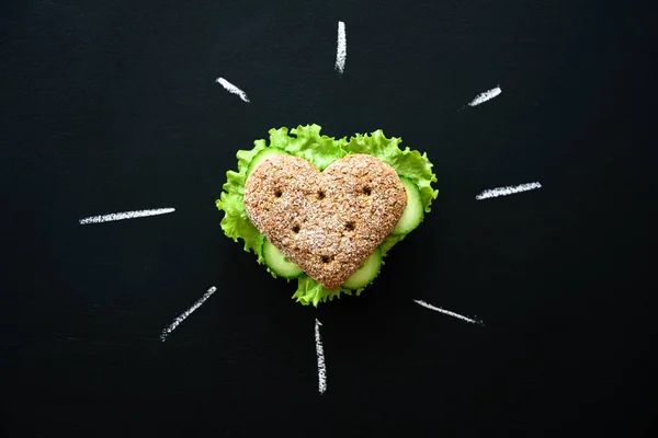 Healthy heart shape sandwich with salad and cucumbers. Dieting concept. Blackboard background