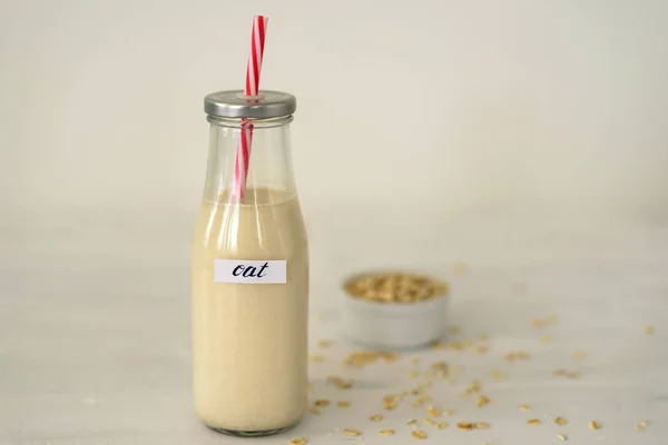 Glass bottle of oat milk on white background. Bowl with oatmeal flakes near it