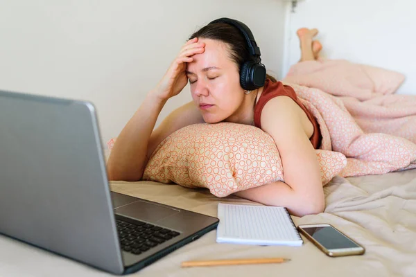 Smiling Woman working on laptop from home in bed. Real life, office in bedroom. She is tired and stress
