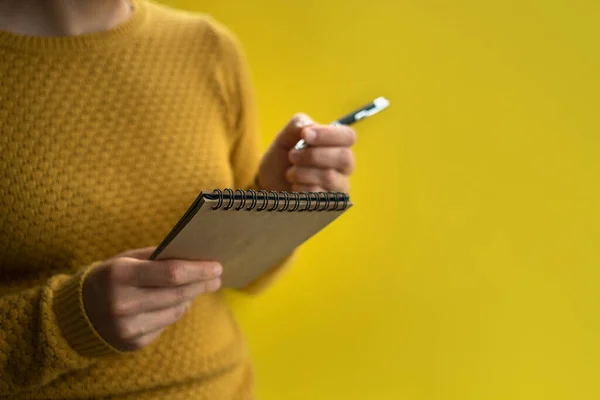 Woman Writing by left hand in notepad. Left hander day concept. In yellow sweater