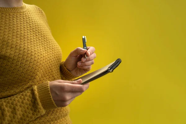 Woman Writing by left hand in notepad. Left hander day concept. In yellow sweater