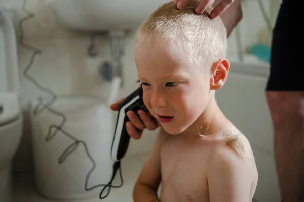 Father making haircut for son at home with haircut machine in bathroom