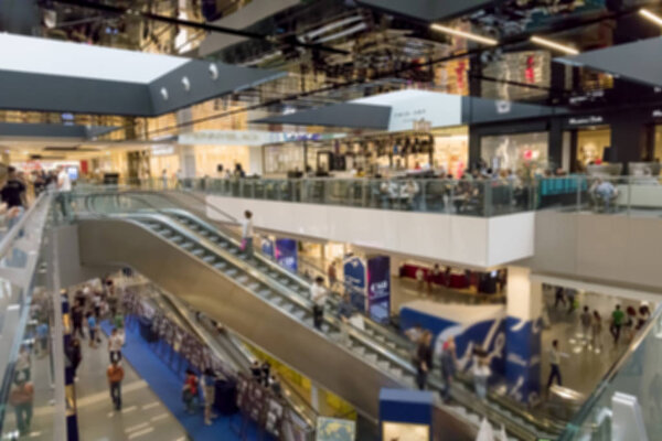 People go shopping inside the shopping center. The spaces with the various shops are developed on several floors connected by long escalators. blurred, unrecognizable.