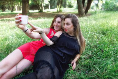 İki kız çimlere uzanmış bir selfie birlikte ve gülümseme ver. Park açık yeşil arka planda.