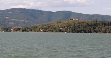 Ada yavaş yavaş yaklaşıyor, Maggiore adasının kıyısında, İtalya'da Trasimeno gölü üzerinde. Ada bitki örtüsü açısından zengin dir ve bulutlu gökyüzü yoğun mavi, gölün suyu gibi.