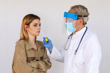 Doktor, salgının yayılmasına neden olan SARS-CoV-2 virüsünü araştırmak için genç bir kadının burun deliğinden örnek aldı..