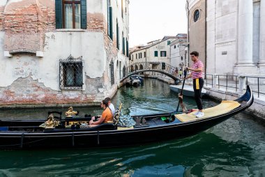 Venedik, İtalya - 1 Ağustos 2020: Gondolcu gondoluyla turistleri Venedik 'in en karakteristik ve romantik yerlerini aramak için şehrin küçük kanallarından geçirir..