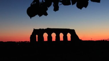 Kırmızıya dönen gökyüzü ile harika bir gün batımı. Antik Roma su kemerinin kalıntılarının ön planında.