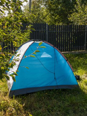 Çitin yanındaki çimlerin üzerinde mavi bir çadır..