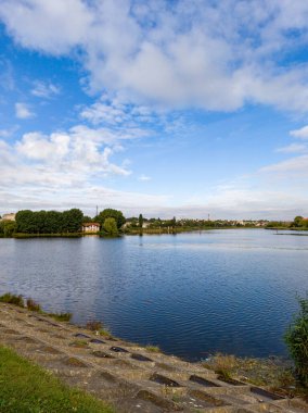 Çimlerle ve ağaçlarla çevrili büyük bir su kütlesi..