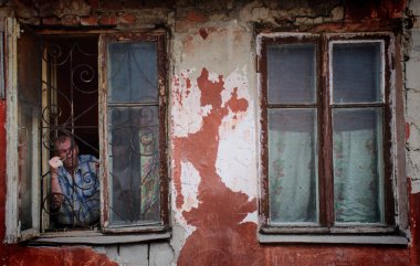 Barnaul,Rusya-1 Mayıs 2019. Fakir bir mahallede eski bir evin penceresinden dışarı bakan bir adam.