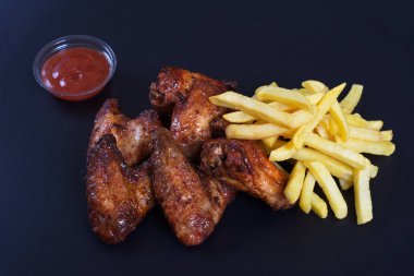 Patates bir garnitür ile kızarmış tavuk kanatları koyu bir arka plan üzerinde yalan