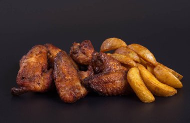 Patates bir garnitür ile kızarmış tavuk kanatları koyu bir arka plan üzerinde yalan