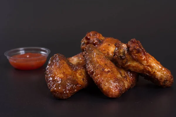 Fried chicken wings with a side dish of potatoes lie on a dark background