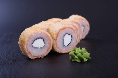 Japon mutfağından deniz ürünleri ve peynirli turuncu rulo koyu bir arka planda yatar.