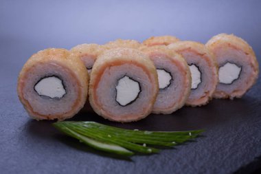 Japon mutfağından deniz ürünleri ve peynirli turuncu rulo koyu bir arka planda yatar.