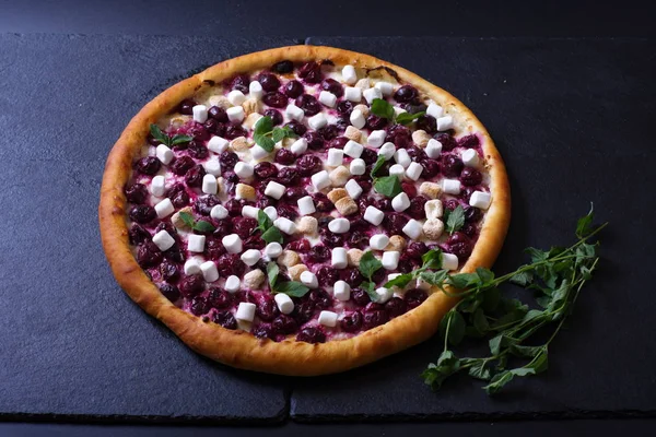 Sweet pizza with marmalade and fruit lies on a black background