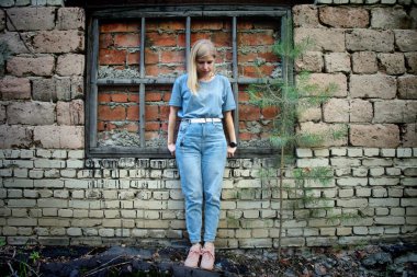 Mavi gözlü sarışın bir kız antik bir binanın yıkıntılarına karşı duruyor.