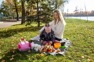 Merhaba Ekim. Anne ve kızı sonbahar şehir parkında yürüyorlar. Ebeveyn ve küçük çocuk dışarıda eğleniyor.