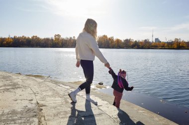 Merhaba Ekim. Anne ve kızı sonbahar şehir parkında yürüyorlar. Ebeveyn ve küçük çocuk dışarıda eğleniyor.
