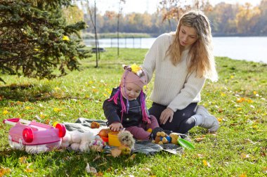 Merhaba Ekim. Anne ve kızı sonbahar şehir parkında yürüyorlar. Ebeveyn ve küçük çocuk dışarıda eğleniyor.