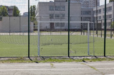 Okul bölgesindeki yeşil çitlerin arkasında futbol oynamak için çim sahası. Yeşil çimenli futbol sahasına yakın çekim