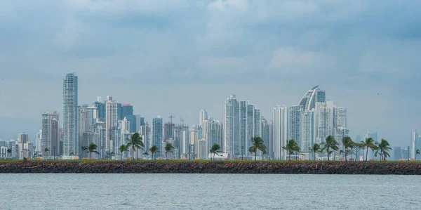Tropical Panama City skyline as storm approaches. Hot humid typical day as another rainstorm brews quickly over the city skyline.  Tall buildings shimmer in heatwaves rising in humid air.  People walking or enjoying the day on Panama Canal jetty park