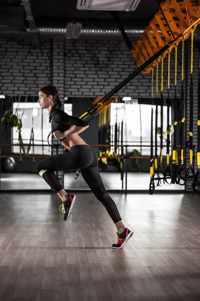 TRX fitness kayışları ile eğitim güzel fitness kadın. Spor salonunda egzersiz süspansiyon