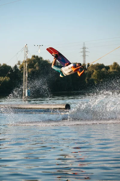 Man makes an extreme jump on wakeboarding, around there are a lot of splashes and splashes of water.