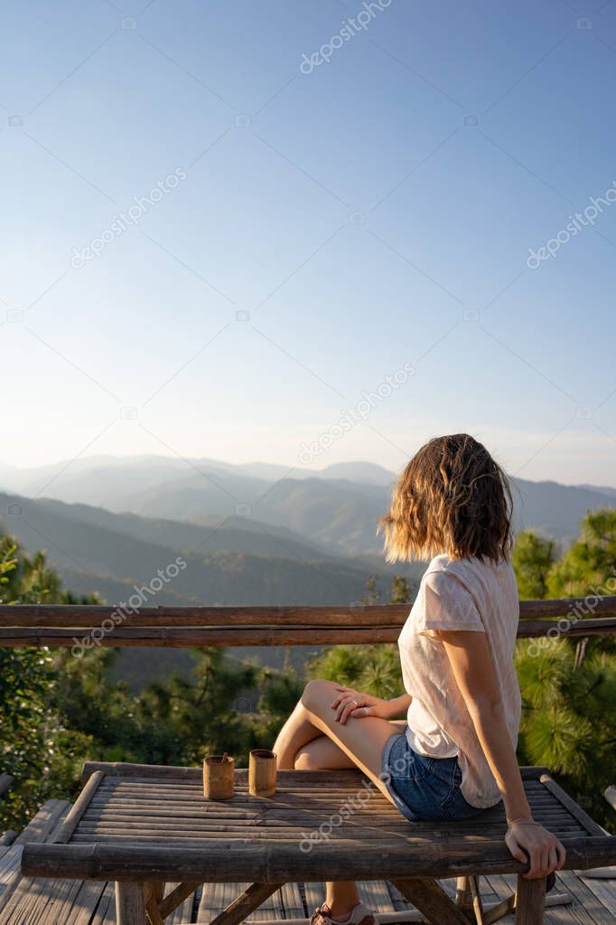 Young girl sitting on a bench with a mountain view at sunset 