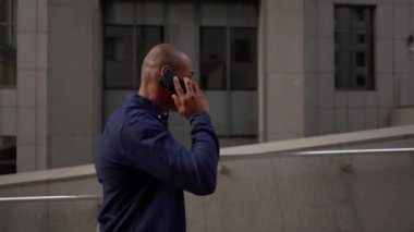 Dizüstü bilgisayarlı kel bir erkeğin merdivenlerden çıkıp cep telefonuyla konuşmasını gösteren bir fotoğraf.