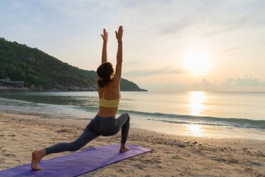 Kadın yoga yapıyor ve gün doğumunda esneme hareketleri yapıyor.