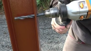 Metal inşaata metal çit döşeyen bir adam. Matkapla ve vidayla metal bir çit yapmak. Elinin ve aletin kapalı konsepti.