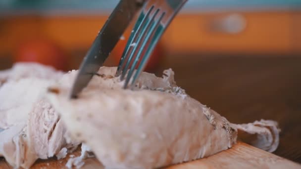 Mujer corta filete de pollo cocido a mano en una tabla de cortar con un tenedor y un cuchillo. — Vídeo de stock