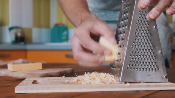 Uomo mano strofina formaggio duro su una grattugia di metallo. Cucina casalinga. Primo piano. — Video Stock