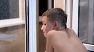 Meraklı Gülümseyen Çocuk Balkonda Pencereden dışarı bakar ve birini izler.