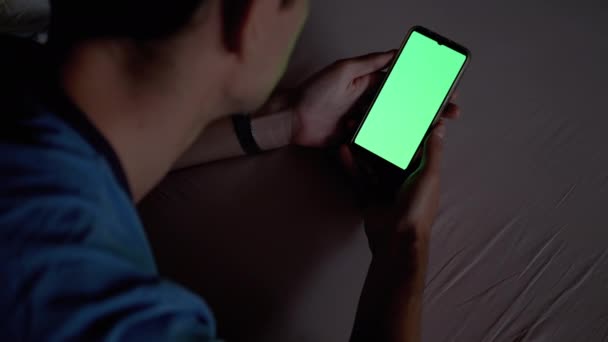 Homme dans l'obscurité sur lit tient et examine Smartphone avec écran tactile vert. — Video