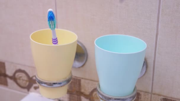 Lanza un cepillo de dientes sucio a una taza de plástico azul en el baño. Primer plano. 4k — Vídeos de Stock