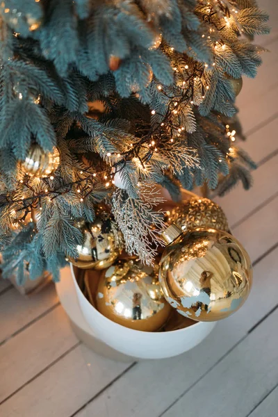 box with shiny baubles on wooden floor near beautiful Christmas tree decorated lights garland