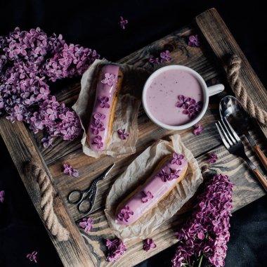 içecek fincan, tatlı eclairs ve koyu arka plan üzerinde mor çiçekler ile düzenleme