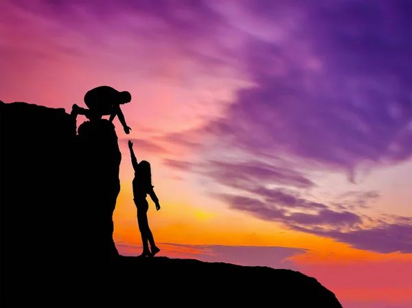 Silhouettes of two people climbing on mountain and helping.