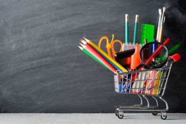 Ayakta boş yazı tahtası yakınındaki küçük alışveriş sepeti ile çeşitli okul malzemeleri.