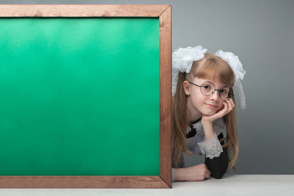 Smiling female kid with tails and glasses presenting green chalkboard with copy space