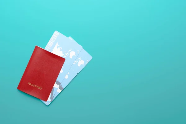 Two plane tickets lying in passport with red cover on left side of turquoise background